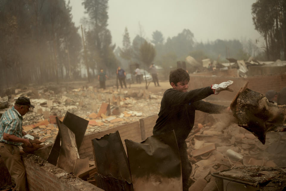 People clear debris after a wildfire swept through the area in Santa Ana, Chile, Saturday, Feb. 4, 2023. Forest fires are spreading in southern and central Chile, triggering evacuations and the declaration of a state of emergency in some regions. (AP Photo/Matias Delacroix)