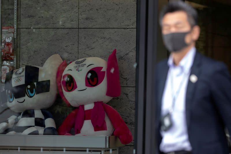 A man wearing a protective face mask, following an outbreak of the coronavirus disease (COVID-19), walks past Tokyo 2020 Olympic Games mascot Miraitowa and Paralympic mascot Someity plushies at a building in Tokyo