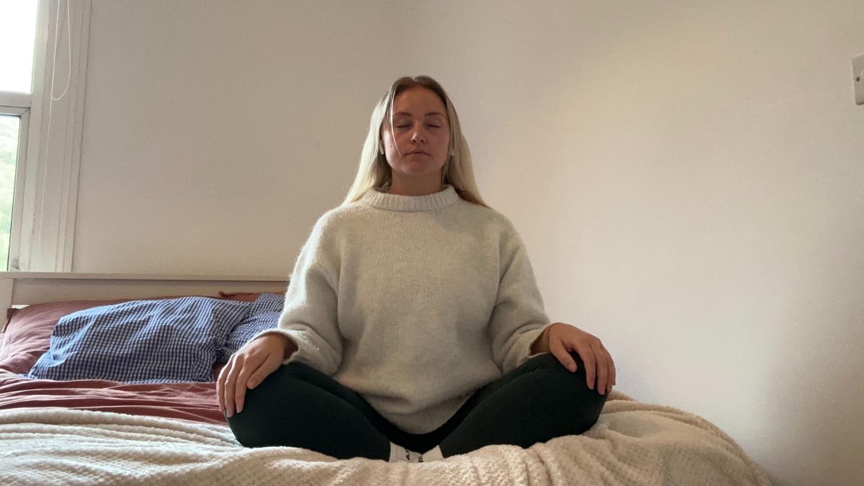  Woman meditating on bed in cross-legged position. 