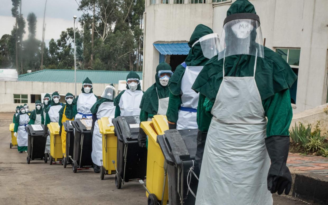 Cleaning staff in personal protective equipment (PPE) carry lidded trash boxes in a line to minimize contamination after collecting PPEs used by doctors who treated patients infected with the COVID-19 novel coronavirus in the intensive care unit (ICU) at Saint Petros Hospital in Addis Ababa, - AFP