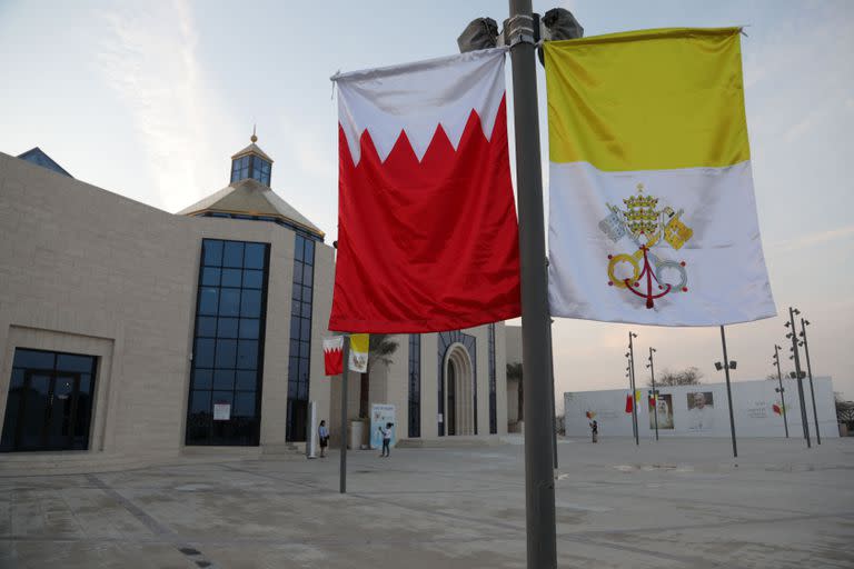 Las banderas de Bahréin (izq.) y del Vaticano cuelgan de un poste de luz, frente a la catedral de Nuestra Señora de Arabia en Awali, al sur de la capital bahreiní, Manama, el 1 de noviembre de 2022, antes de la visita del Papa al reino.