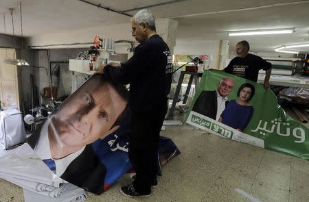 Workers hold freshly printed campaign banners in Arabic that depict Isaac Herzog (L), who heads the centre-left Zionist Union alliance with former cabinet minister Tzipi Livni, and Zehava Galon (R), chair of the left-wing Meretz party, at a printing factory in the Arab village of Baqa al-Gharbiya in northern Israel March 2, 2015. REUTERS/Ammar Awad