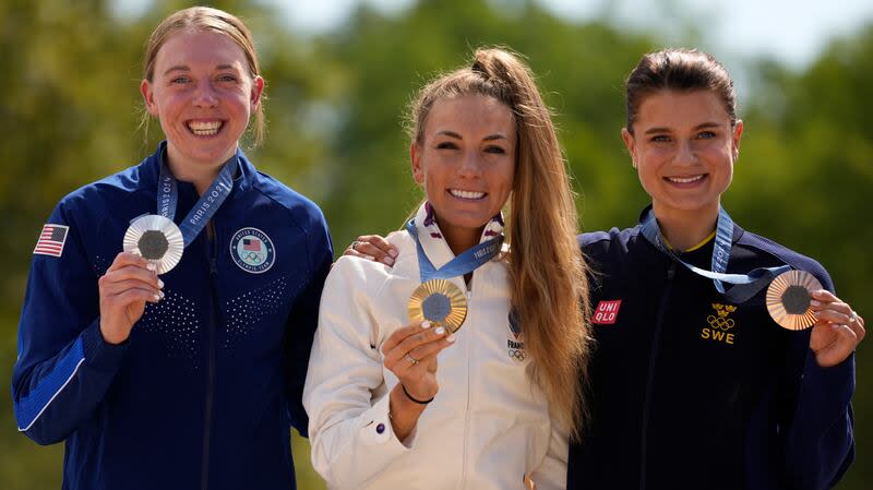 Pauline Ferrand Prevot, of France, centre, winner of the women's mountain bike cycling event, shows her gold medal flanked by silver medallist Haley Batten, of United States, left, and bronze medallist Jenny Rissveds, of Sweden, at the 2024 Summer Olympics, Sunday, July 28, 2024, in Elancourt, France. | George Walker IV