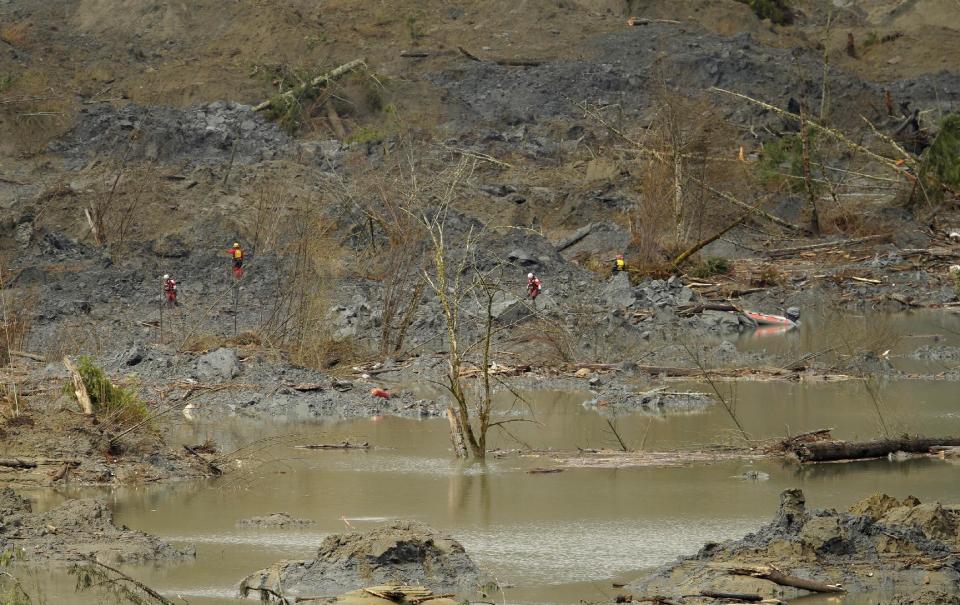 Search workers wearing red are dwarfed by the mud and debris filled landscape they were searching Thursday, March 27, 2014, where a massive mudslide struck Saturday near Darrington, Wash. The searchers shown had to use a boat to reach the area shown. (AP Photo/Ted S. Warren, Pool)