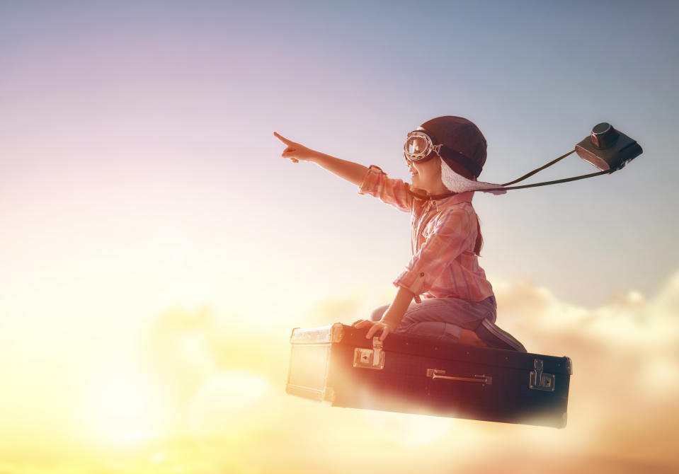 Child riding on a flying suitcase above the clouds.