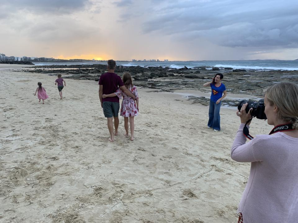 A family walking on the beach while a photographer takes shots of them.