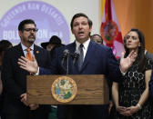 FILE- In this May 9, 2019 file photo. Florida Gov. Ron DeSantis, second from right, speaks during a bill signing ceremony at the William J. Kirlew Junior Academy, in Miami Gardens, Fla. A surge of asylum-seeking families has been straining cities along the southern U.S. border for months, but now the issue is flowing into cities far from Mexico, where immigrants are being housed in airplane hangars and rodeo fairgrounds and local authorities are struggling to keep up with the influx. (AP Photo/Lynne Sladky, File)