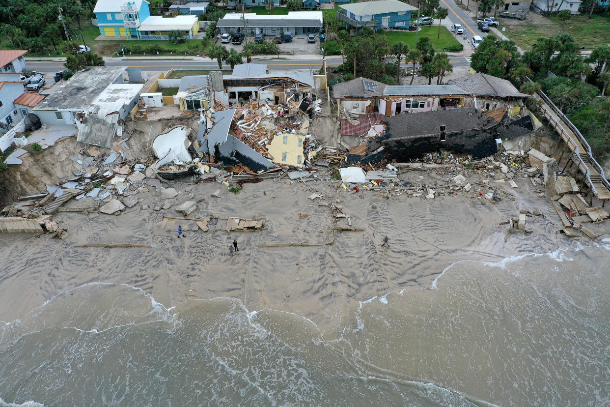 An aerial view of the ocean lapping up to a half-dozen homes partially toppled onto the beach.