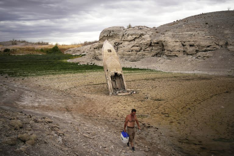 Un hombre camina junto a un bote anteriormente hundido que se eleva en el aire con la popa enterrada en el lodo a lo largo de la costa del lago Mead en el área recreativa nacional del lago Mead cerca de Boulder City, Nevada, el 22 de junio de 2022