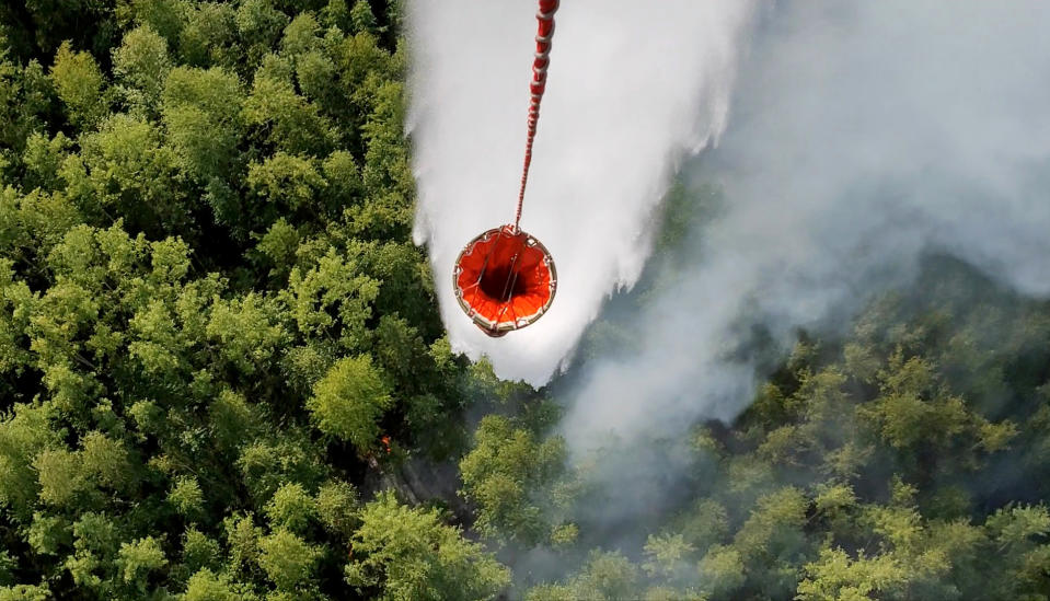 A still image, taken from a video footage shows a helicopter dropping water over a burning forest in Krasnoyarsk region, Russia August 4, 2019. Video footage taken August 4, 2019. REUTERS via Reuters TV