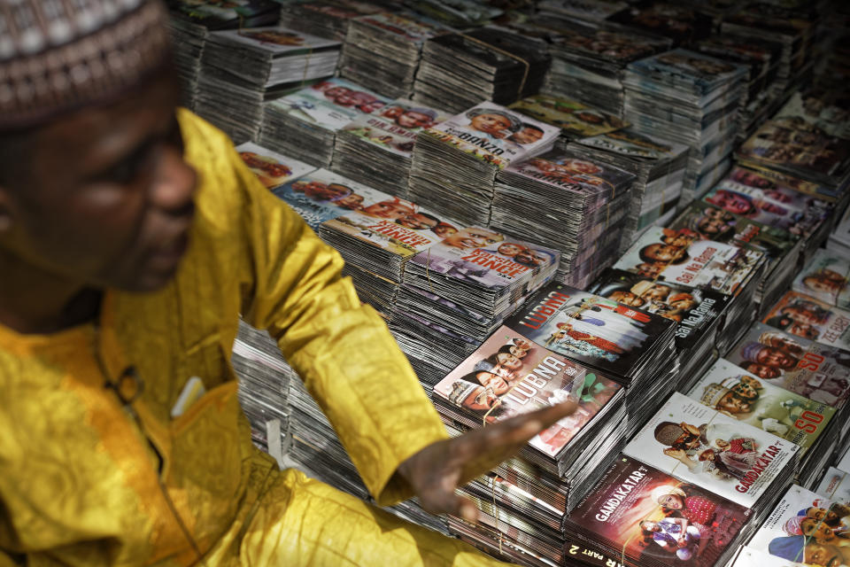 In this photo taken Tuesday, Feb. 19, 2019, shopkeeper Abdulkarim Abdulmumin sits by the piles of Hausa-language DVDs he sells in the market in Kano, northern Nigeria. Faced with an election that could spiral into violence, some in the popular Hausa-language film industry known as Kannywood assembled this week to shoot an urgent music video appealing to the country for peace. (AP Photo/Ben Curtis)