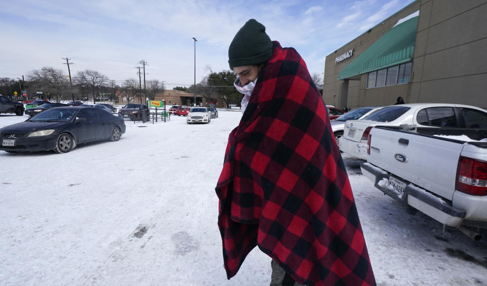 Cody Jennings utiliza un cobertor para mantenerse caliente afuera de una tienda en Dallas, el martes 16 de febrero de 2021. (AP Foto/LM Otero)