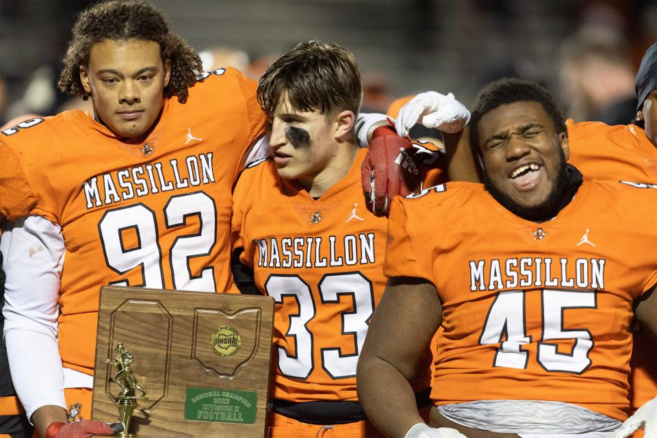 Massillon's Chase Bond (92), Cody Fair (33) and Michael Wright Jr. (45) celebrate with the regional championship trophy Nov. 17 after beating Green 31-6 in North Canton.