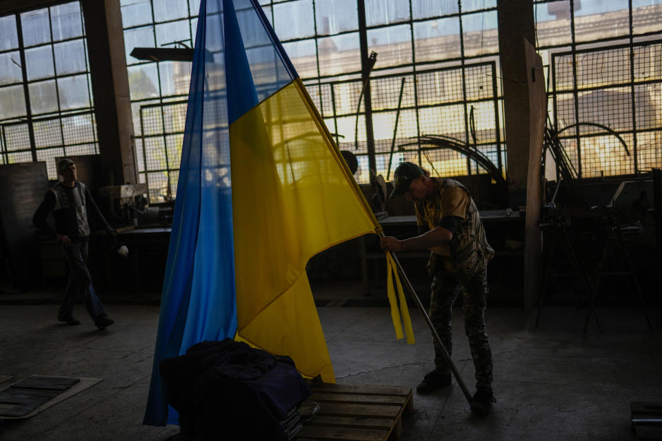 A volunteer places a Ukraine flag on a metal bar at a facility producing material for Ukrainian soldiers in Zaporizhzhia, Ukraine, Friday, May 6, 2022. An old industrial complex in the southeastern Ukrainian riverside city of Zaporizhzhia has become a hive of activity for volunteers producing everything from body armor to camouflage nets, anti-tank obstacles to heating stoves and rifle slings for Ukrainian soldiers fighting the Russian invasion. (AP Photo/Francisco Seco)