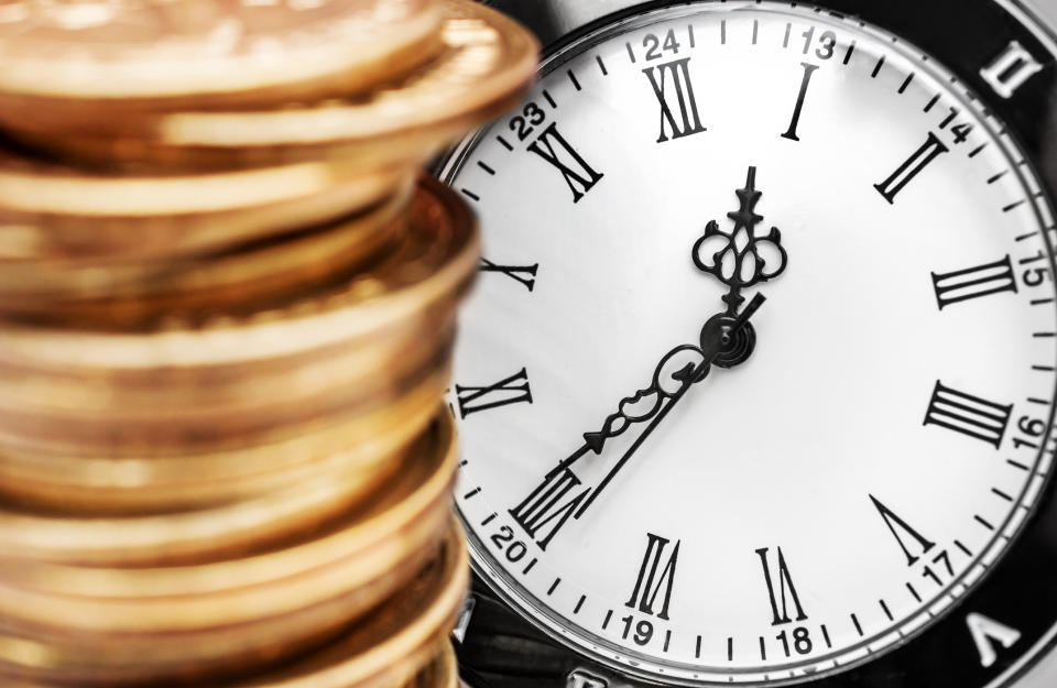 A stack of gold coins in front of a clock