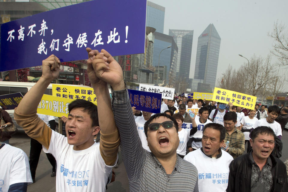 FILE - In this Tuesday, March 25, 2014 file photo, Chinese relatives of passengers onboard the missing Malaysia Airlines plane, flight MH370, shout in protest as they march towards the Malaysia embassy in Beijing, China. Authorities have been forced on the defensive by the criticism, the most forceful of which has come from a group of Chinese relatives who accuse them of lying about - or even involvement in - the disappearance of Flight 370. The blue placard reads: "We won't leave or ditch you, we will wait right here." (AP Photo/Ng Han Guan, File)