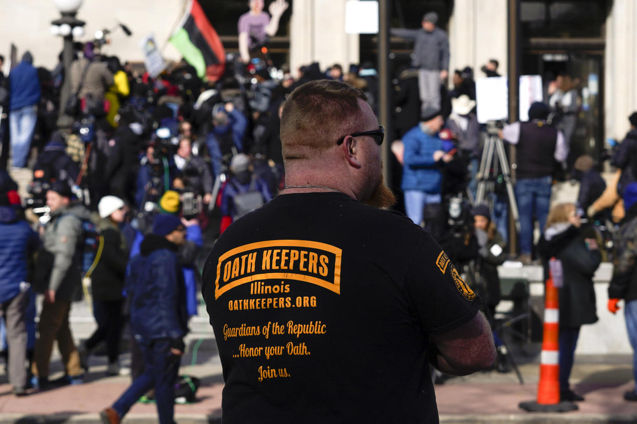 FILE - A man wearing an Oath Keepers shirt stands outside the Kenosha County Courthouse, Nov. 19, 2021 in Kenosha, Wis. A new report says that the names of hundreds of U.S. law enforcement officers, elected officials and military members appear on the leaked membership rolls of a far-right extremist group that's accused of playing a key role in the Jan. 6, 2021, riot at the U.S. Capitol. The Anti-Defamation League Center on Extremism pored over more than 38,000 names on leaked Oath Keepers membership lists to find more than 370 people it believes are currently working in law enforcement agencies. (AP Photo/Paul Sancya, File)