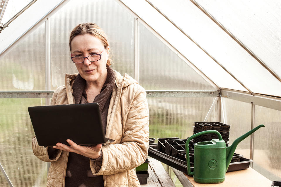 mature woman with glasses and laptop in greenhouse