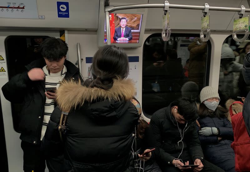 Passengers are seen next to a screen broadcasting news of Chinese President Xi Jinping addressing a New Year's Eve speech, on a subway train in Beijing