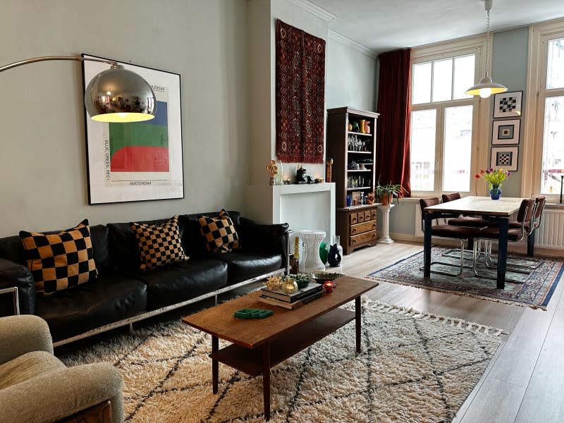 Living room and dining room with black leather vintage sofa, vintage rugs, and vintage art on the walls