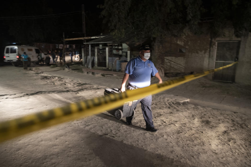 A forensic worker leaves a crime scene after inspecting the body of a man fatally shot in the streets of the Rivera Hernandez neighborhood in San Pedro Sula, Honduras, on Nov. 30, 2019. There are police stations in these neighborhoods, but everyone knows who is in charge. The gangs monitor the streets, the police patrols and rival gangs using a complex network of young boys who work in shifts around the clock and report anything suspicious. (AP Photo/Moises Castillo)