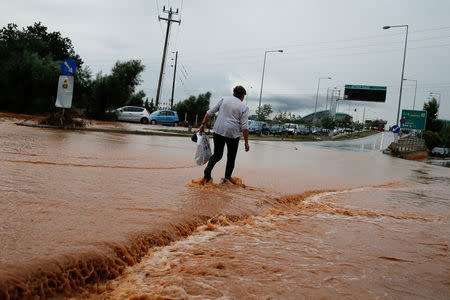 A woman tries to cross a flooded road, following flash floods which hit the town of Magoula, Greece, June 27, 2018. REUTERS/Costas Baltas