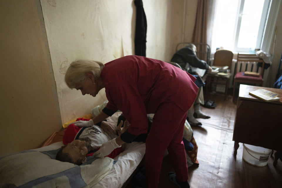 A nurse cares for a man in a shelter for injured and homeless people in Izium, Ukraine, Monday, Sept. 26, 2022. A young Ukrainian boy with disabilities, 13-year-old Bohdan, is now an orphan after his father, Mykola Svyryd, was taken by cancer in the devastated eastern city of Izium. (AP Photo/Evgeniy Maloletka)