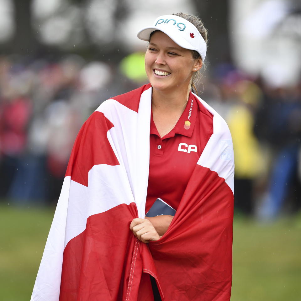 Canada's Brooke Henderson is wrapped in a Canadian flag as she celebrates her win at the Women's Canadian Open golf tournament in Regina, Saskatchewan, Sunday Aug. 26, 2018. (Jonathan Hayward/The Canadian Press via AP)