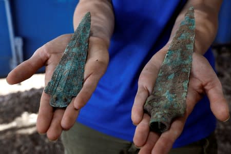 A woman holds an arrowhead and a dagger, part of findings uncovered at a huge prehistoric settlement discovered by Israeli archaeologists in the town of Motza near Jerusalem