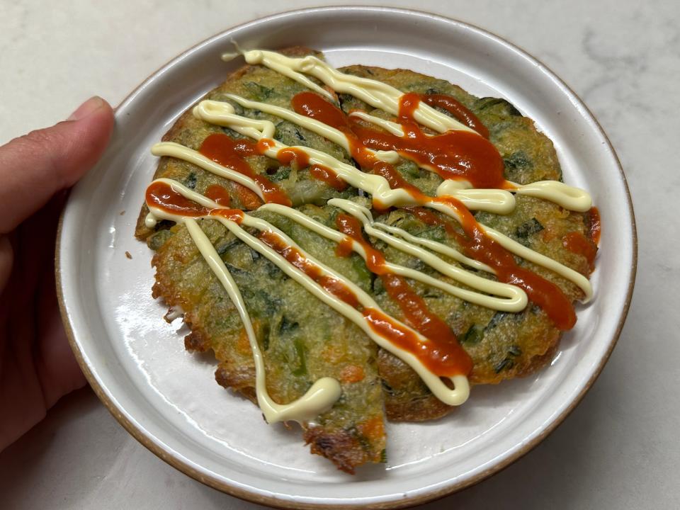 hand holding a plate of scallion pancakes with sauce on top