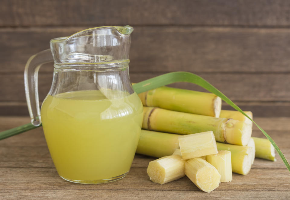 Fresh squeezed sugar cane juice in pitcher with cut pieces cane on wooden background.