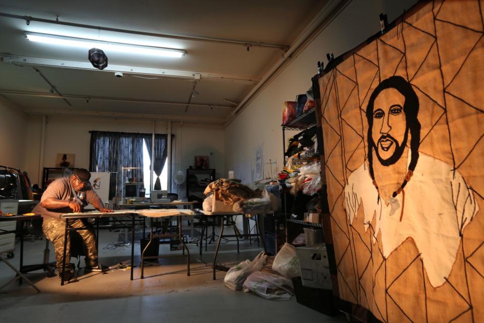 Gary Tyler works on a quilt next to another quilt, which features him as a young man