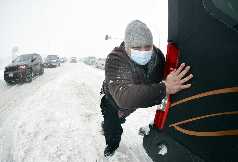 Matt Mittelstaedt, a driver for Missouri Slope Lutheran Care Center, pushes as a Good Samaritan tows the large passenger van he was driving when it got stuck in the snow at the intersection of State Street and Divide in Bismarck, N.D., Tuesday, April 12, 2022. (Mike McCleary/The Bismarck Tribune via AP)