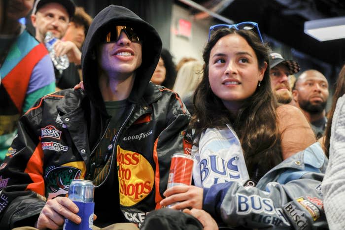 Pete and Chase arm-in-arm as they hold drinks and sit in a crowd at an event