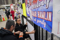 Kayla Adeniji, center, wife of Cincinnati Bengals offensive lineman Hakeem Adeniji, tapes up a sign she made in support of Buffalo Bills safety Damar Hamlin outside UC Medical Center, Thursday, Jan. 5, 2023, in Cincinnati. Hamlin, who remains hospitalized at the center, has shown what physicians treating him are calling "remarkable improvement over the last 24 hours," the team announced on Thursday, three days after the player went into cardiac arrest and had to be resuscitated on the field. (AP Photo/Joshua A. Bickel)