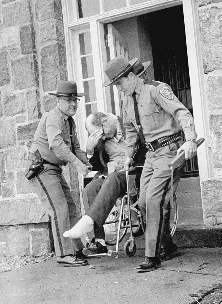 police officers carrying him out on a wheelchair