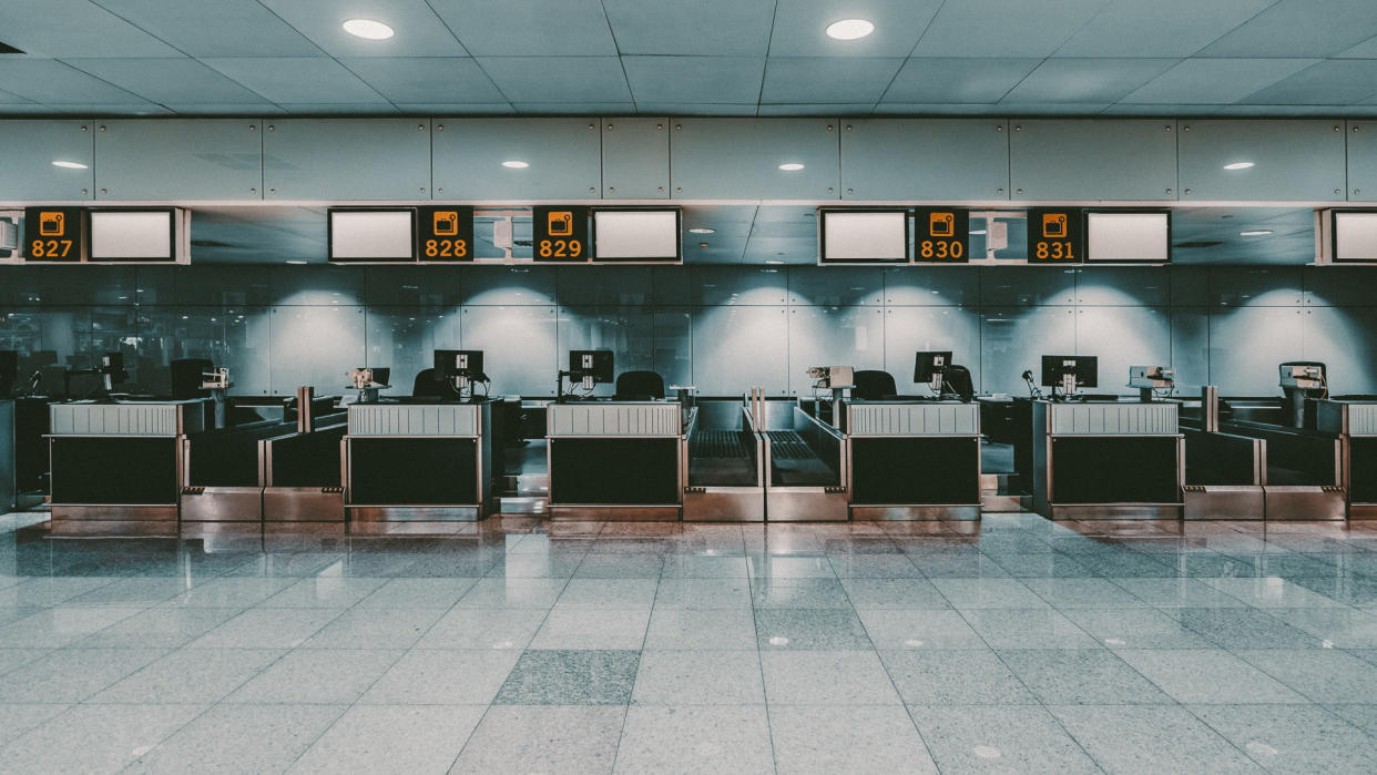 Front view of a check-in area in a modern airport: luggage accept terminals with baggage handling belt conveyor systems, multiple empty white informational LCD screen mockups, indexed check-in desks.