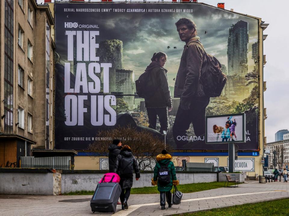 people walk past a billboard for hbo show the last of us