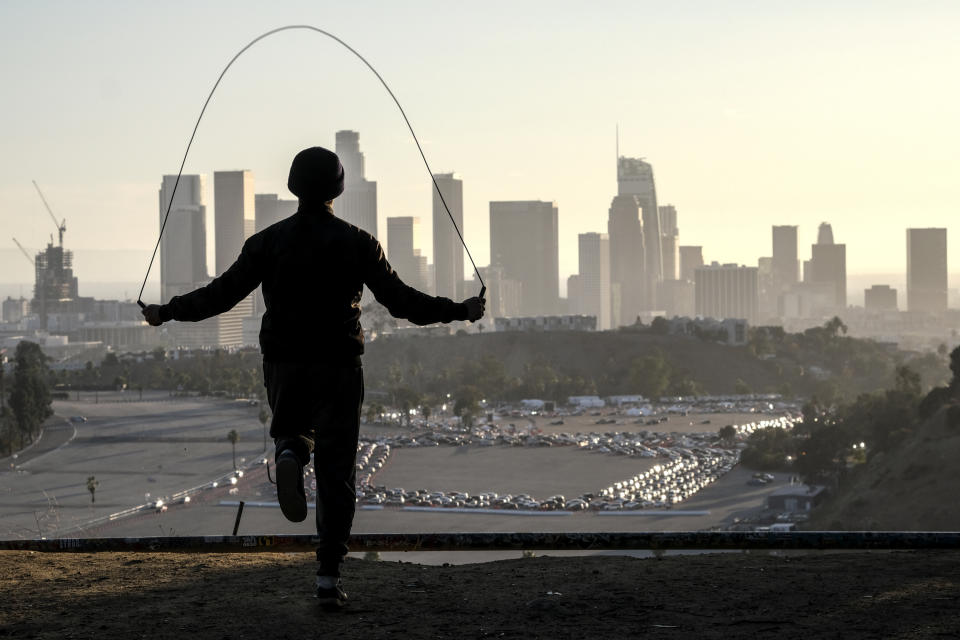 Alex Gonzalez, 19, jumps rope on Angel's Point at Elysian Park as motorists wait in long lines to take a coronavirus test in a parking lot at Dodger Stadium, Monday, Jan. 4, 2021, in Los Angeles. (AP Photo/Ringo H.W. Chiu)