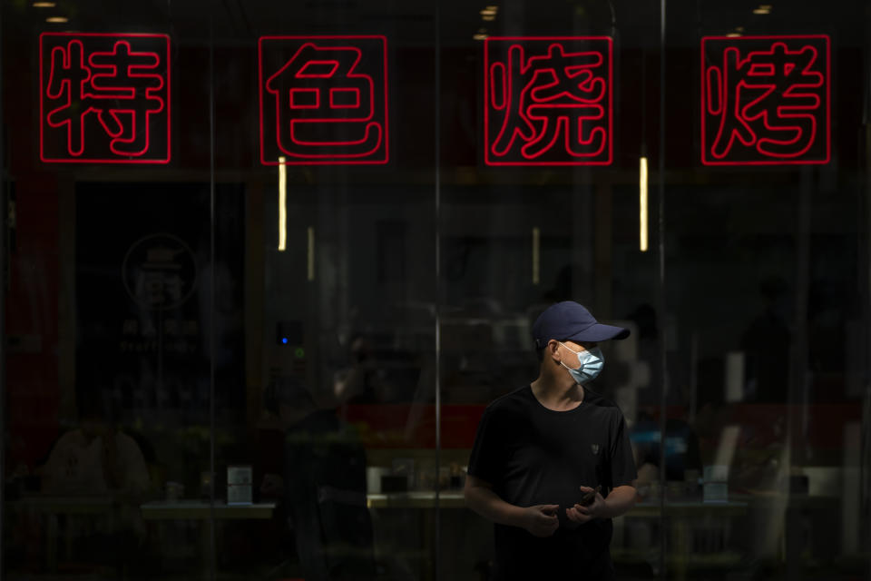 FILE - A man wearing a face mask stands in a beam of sunlight outside of a barbecue restaurant in Beijing, Sept. 8, 2022. The war in Ukraine, the lingering coronavirus pandemic and climate change are putting intense pressure on the world's poorest, the Organization for Economic Cooperation and Development warned.(AP Photo/Mark Schiefelbein)