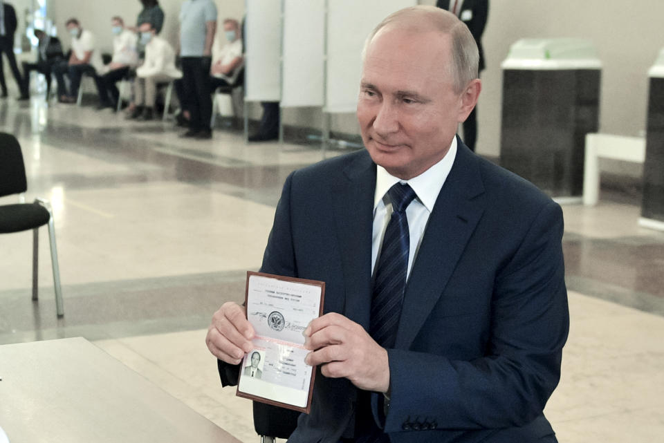 Russian President Vladimir Putin shows his passport to a member of an election commission as he arrives to take part in voting at a polling station in Moscow, Russia, Wednesday, July 1, 2020. The vote on the constitutional amendments that would reset the clock on Russian President Vladimir Putin's tenure and enable him to serve two more six-year terms is set to wrap up Wednesday. (Alexei Druzhinin, Sputnik, Kremlin Pool Photo via AP)