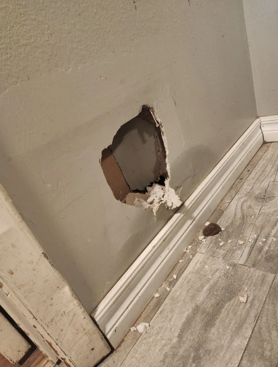 Wall with a hole near a baseboard, with drywall and debris on the floor