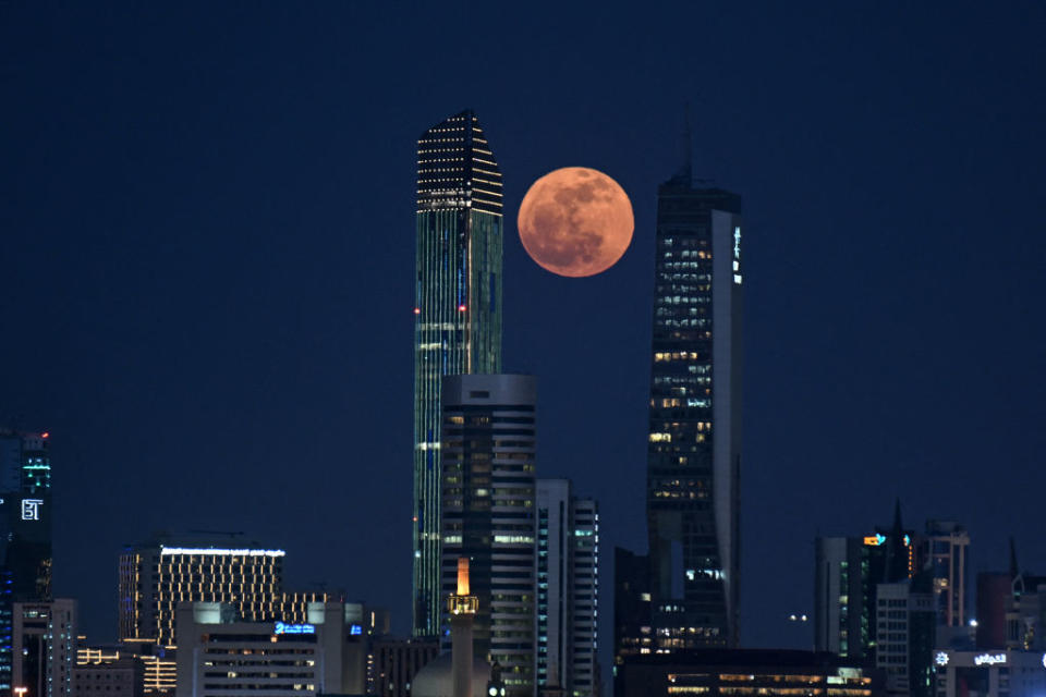 city ​​skyline at night with a full orange, pink moon shining between two large skyscrapers.