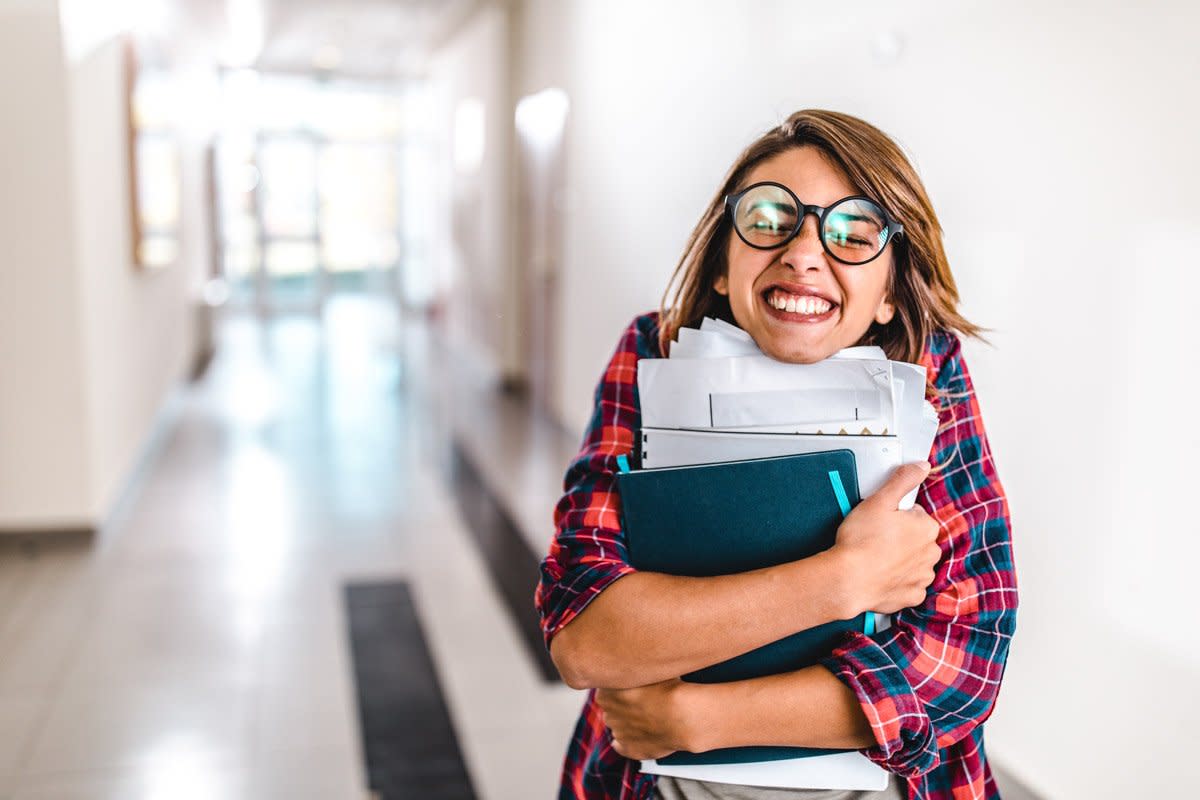 A student smiles while holding paper in a hallway at school. 