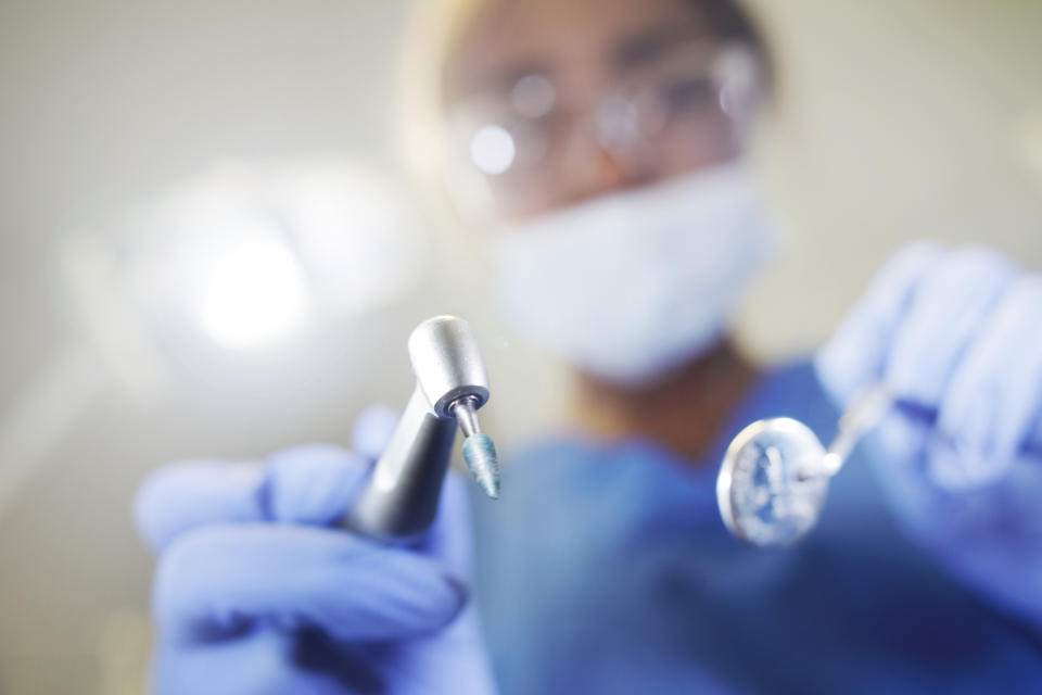 Dentist in scrubs holding dental tools, close-up, from patient's perspective