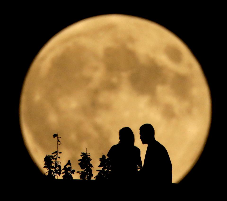 A couple sit on a bluff overlooking the Missouri River as the full harvest moon rises in the distance Sept. 8, 2014, in Kansas City, Mo.