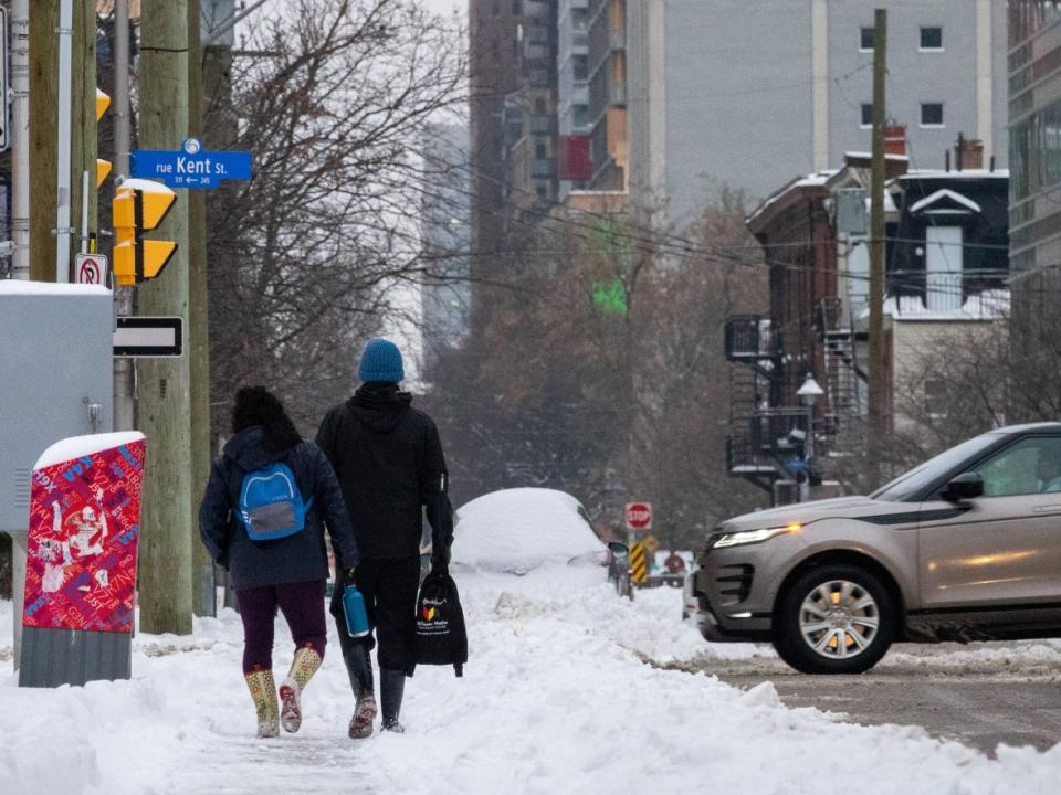 A couple carrying backpacks walk along a snow-covered sidewalk in central Ottawa after Monday's heavy snowfall. (Francis Ferland/CBC - image credit)