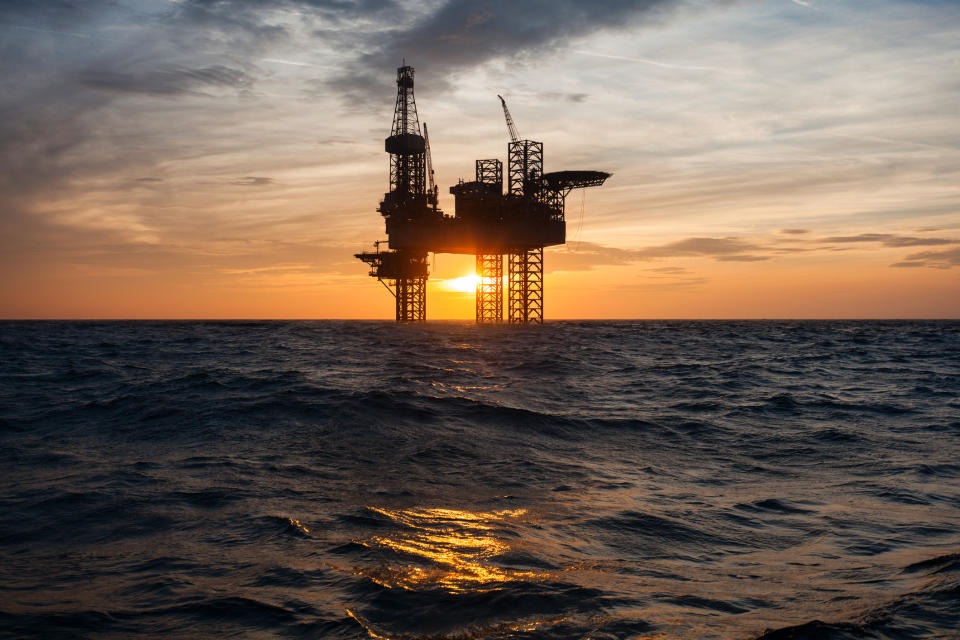 Silhouette of an offshore oil drilling rig with the sun setting in the background.