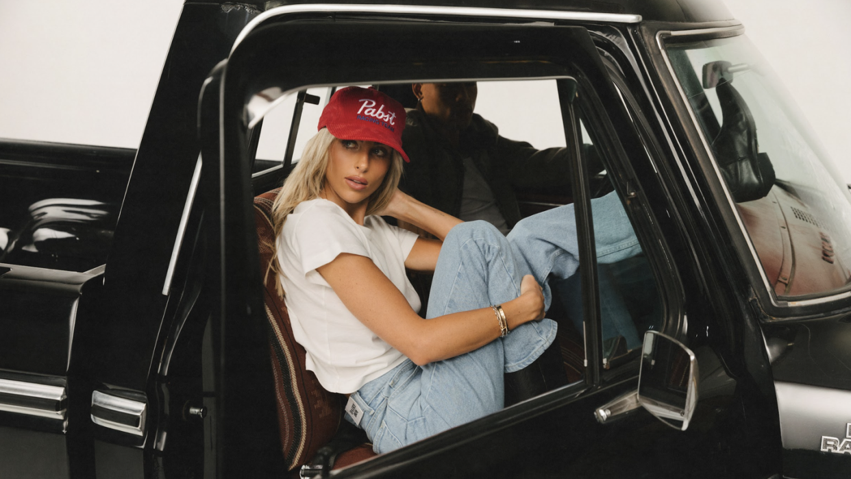 paige lorenze sitting in a black truck wearing blue jeans, a white shirt and a red hat