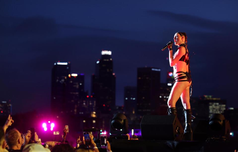 A person performs at night while wearing a two-piece bikini-like black outfit onstage.